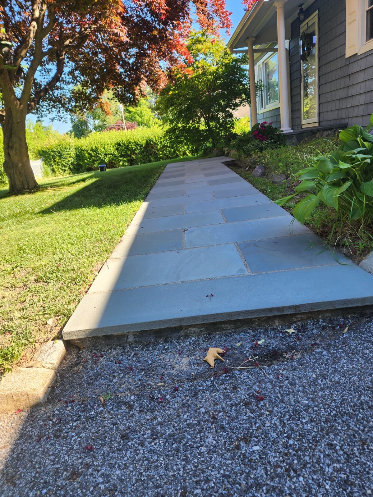 Bluestone walkway bordered by lawn leading along the side of a home