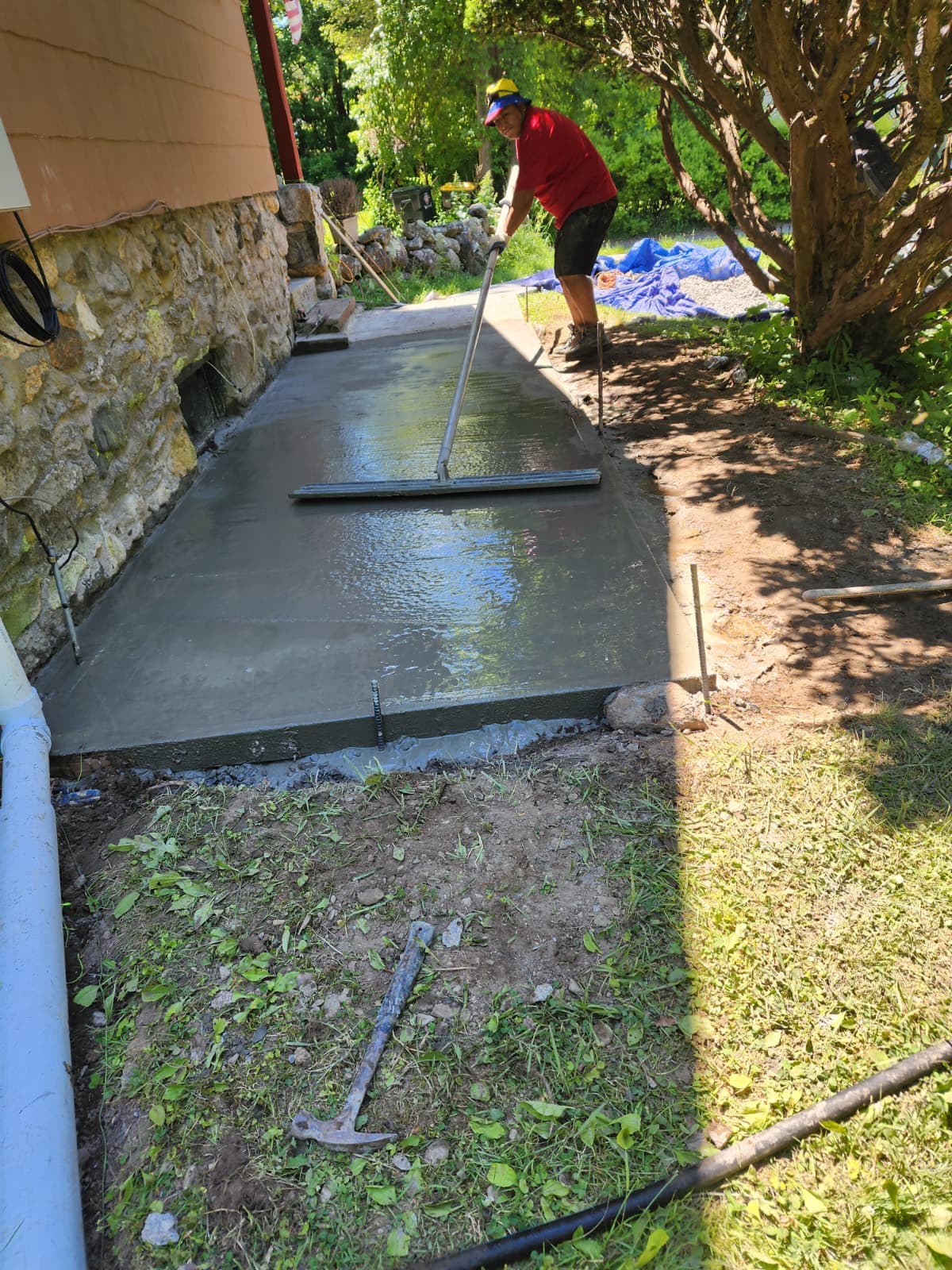 Freshly poured and floated concrete walkway beside a stone foundation