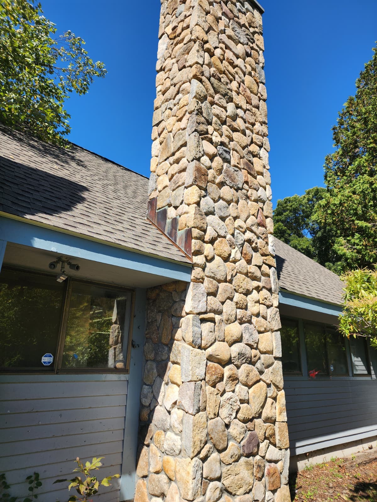 Full-height natural fieldstone chimney veneer against a blue sky